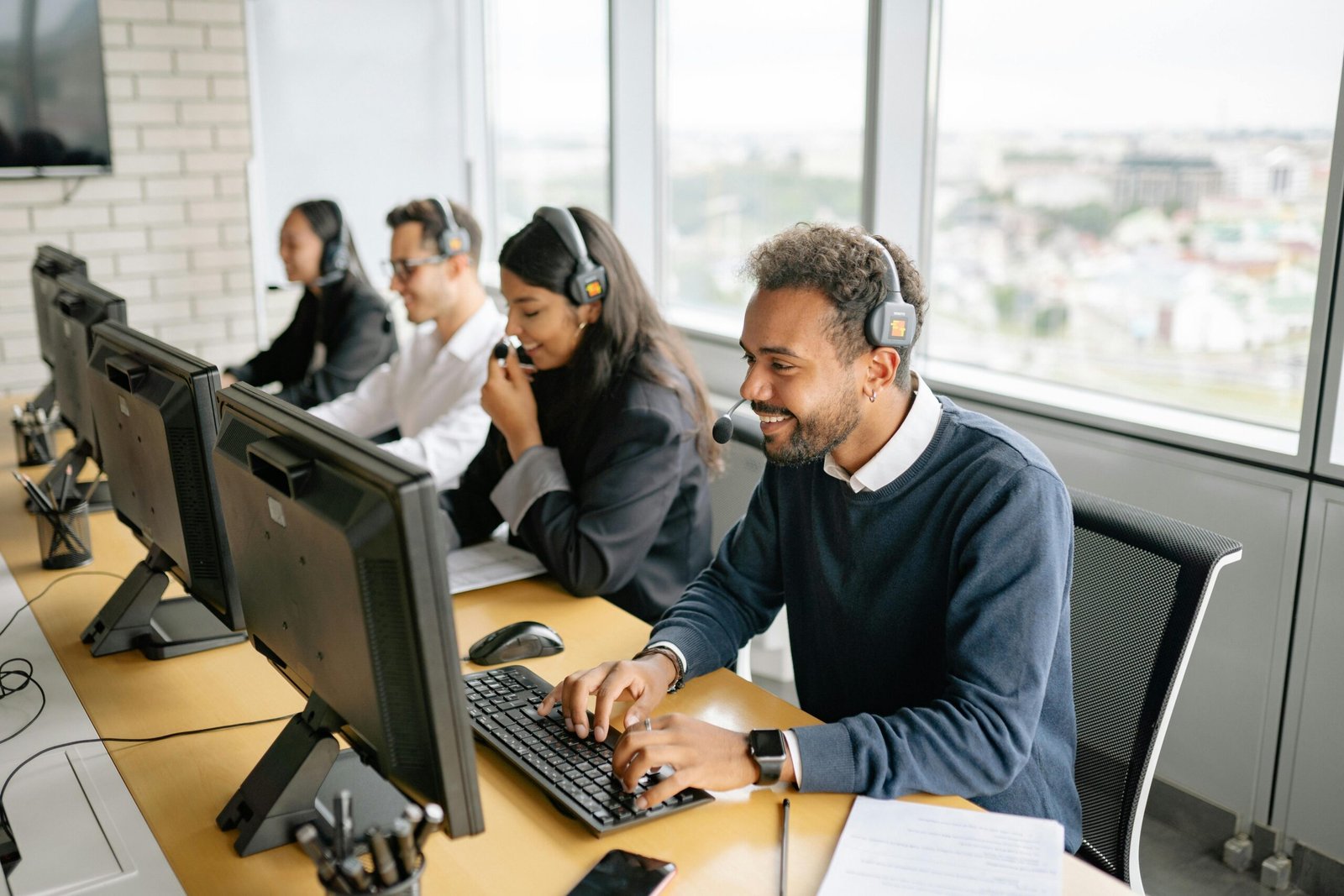 Personas en una oficina hablando por teléfono con auriculares y micrófonos frente a computadoras."