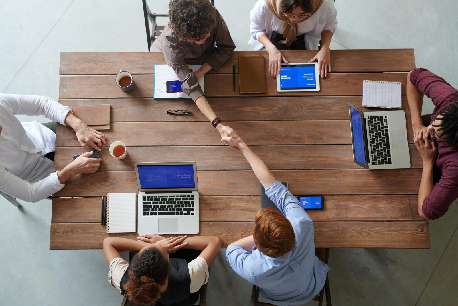 Vista aérea de una mesa de oficina con seis personas sentadas, vestidas formalmente y trabajando en computadoras.