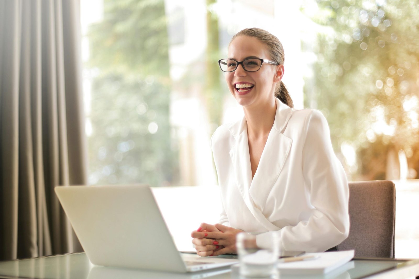 Mujer sonriente en su oficina, vestida con camisa blanca, trabajando en su computadora.