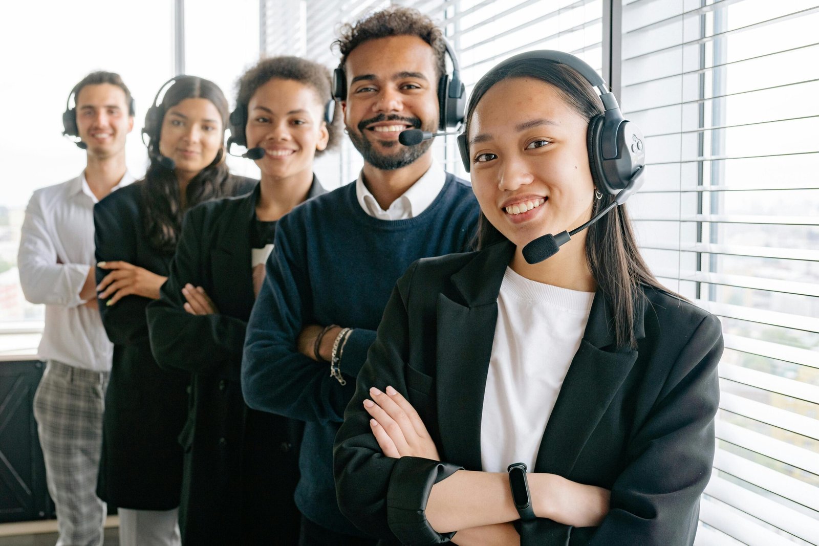 Cinco personas paradas con auriculares y micrófonos, sonriendo mientras posan para la foto en lo que parece ser un call center.