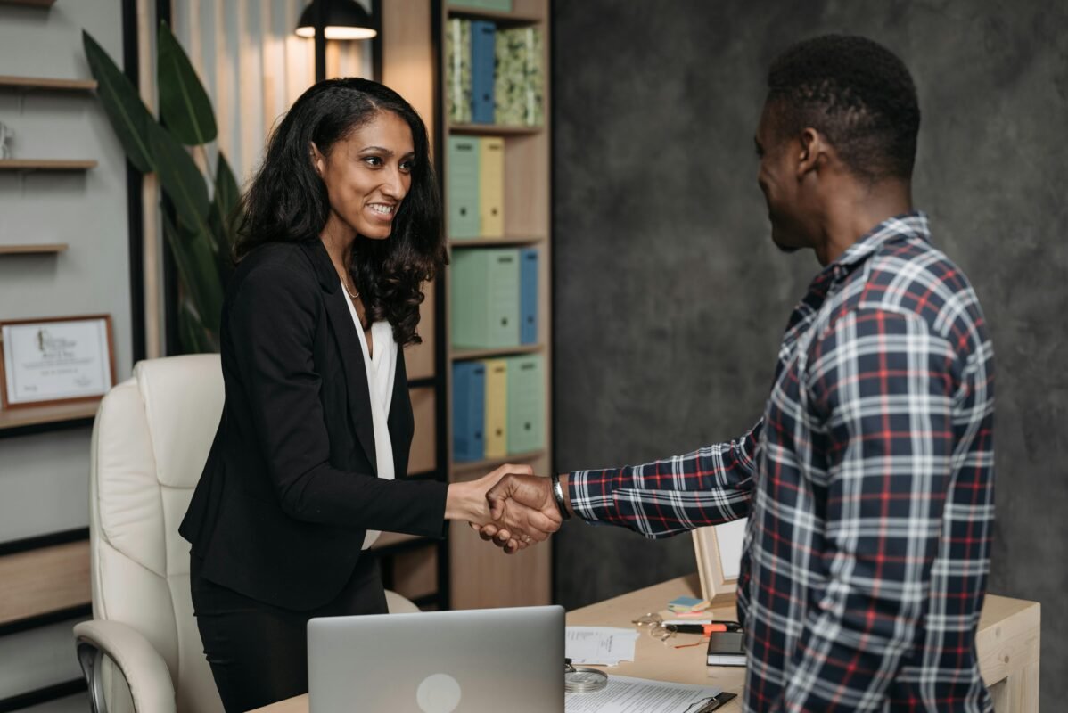 Dos personas en una oficina dándose la mano con una expresión de satisfacción y éxito